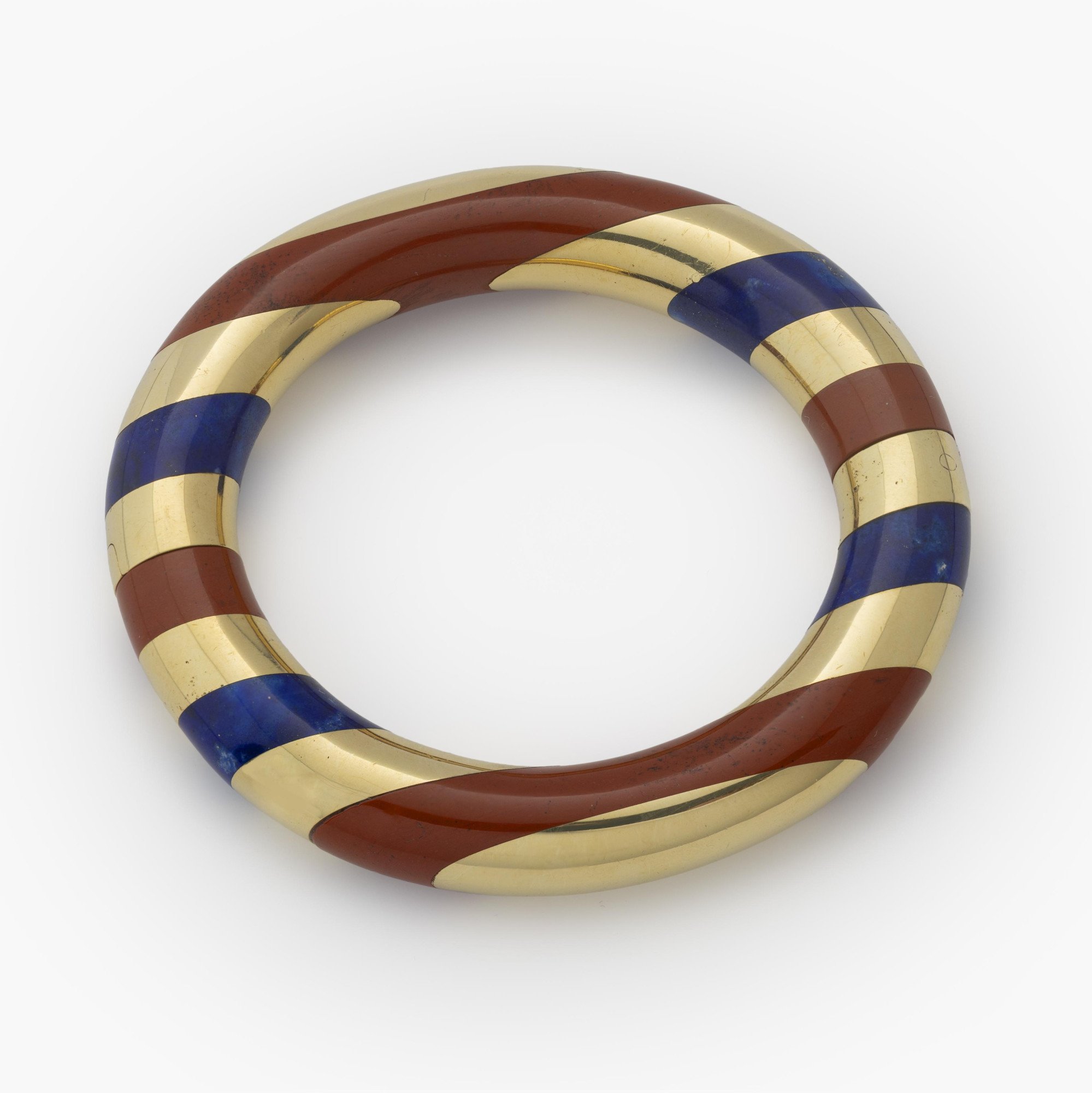 Een achttien karaat geelgouden stijve armband met gesneden lapis lazuli afgewisseld met banden van rode jaspis. Gesigneerd Tiffany & Co., omstreeks 1978.