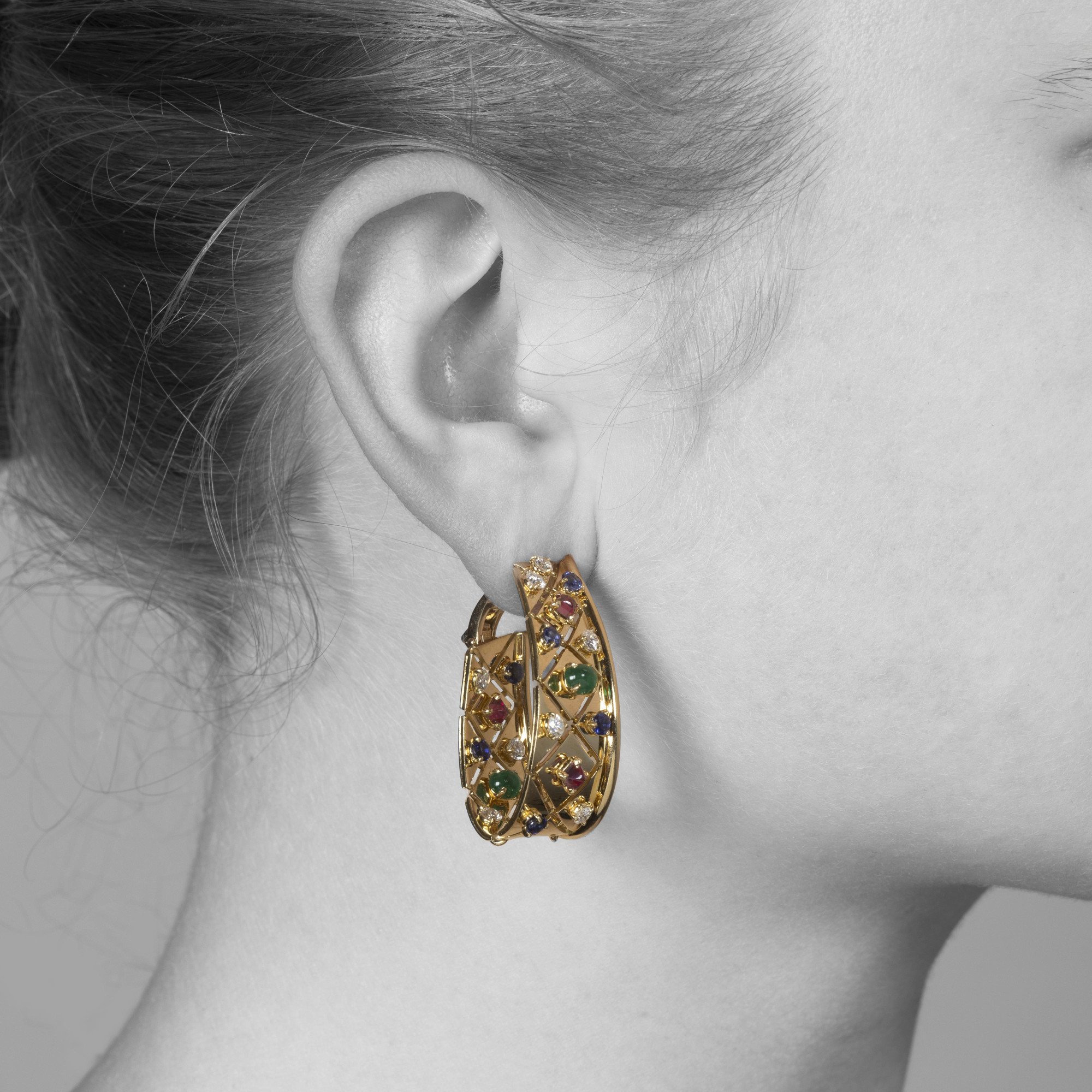 Een paar achttien karaat geelgouden oorbellen, model ´Liberty´, bezet met diamant, saffier, robijn en smaragd. Gesigneerd Cartier, Parijs, ca 1980.