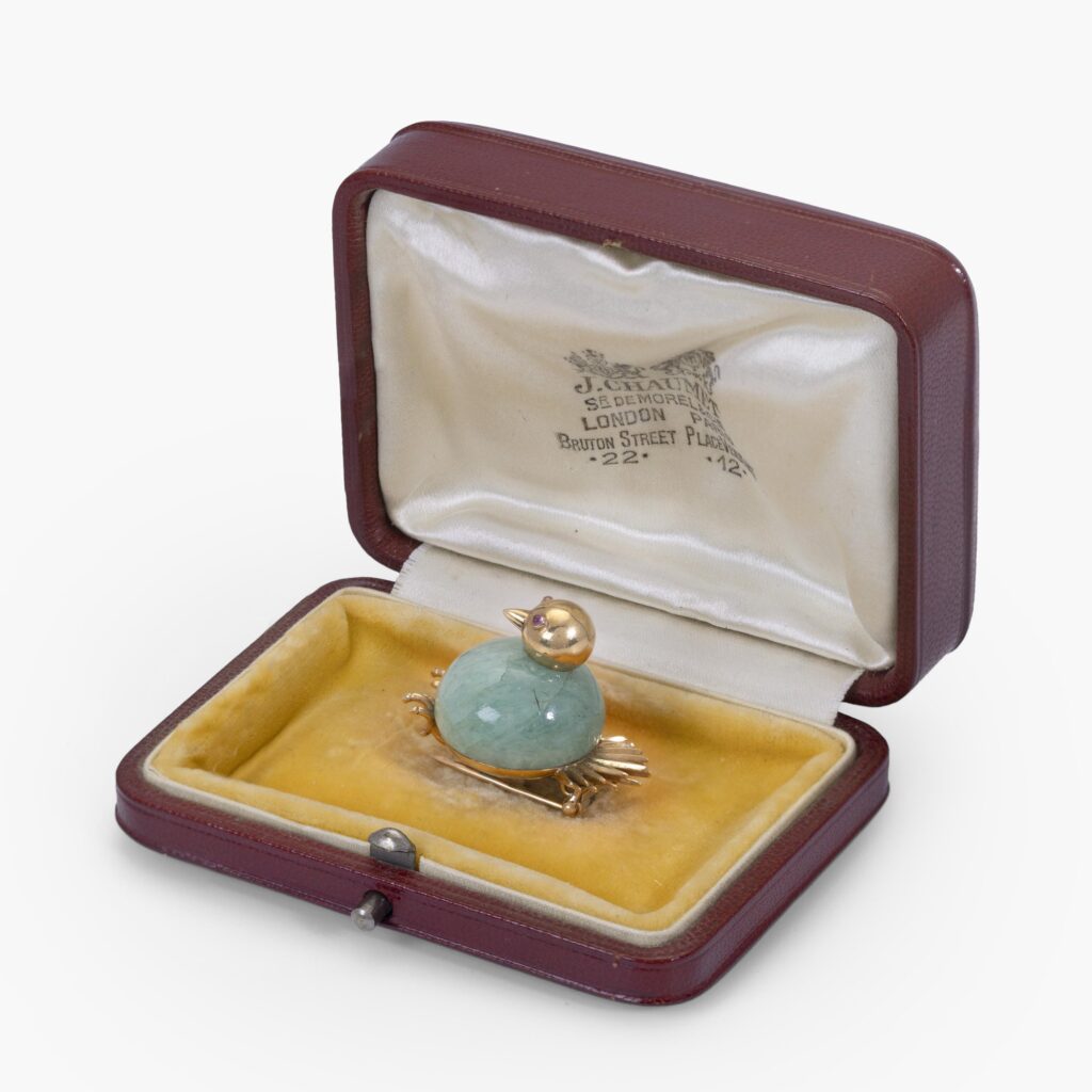 Een achttien karaat geelgouden broche in de vorm van een vogel, het lijf van smaragd, de ogen van robijn. Gesigneerd Chaumet, Parijs. In origineel etui.