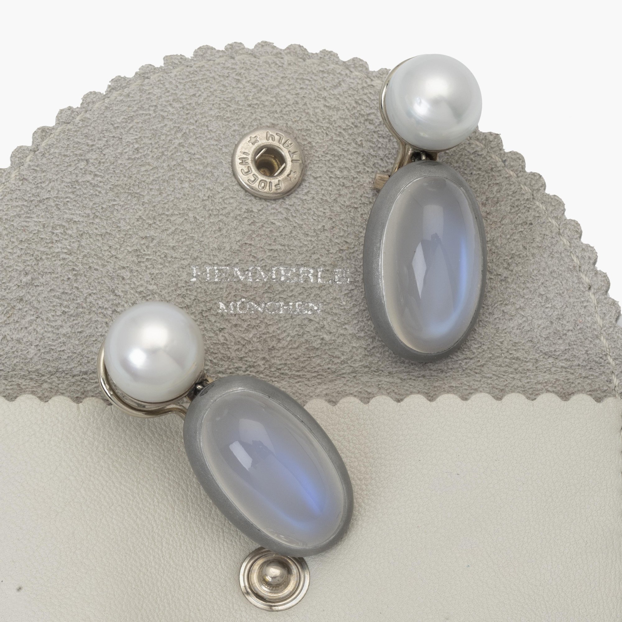 Een paar witgouden oorbellen, bezet met een Zuidzee parel en in aluminium een blauwe maansteen. Gesigneerd Hemmerle, München. Met originele pouch.