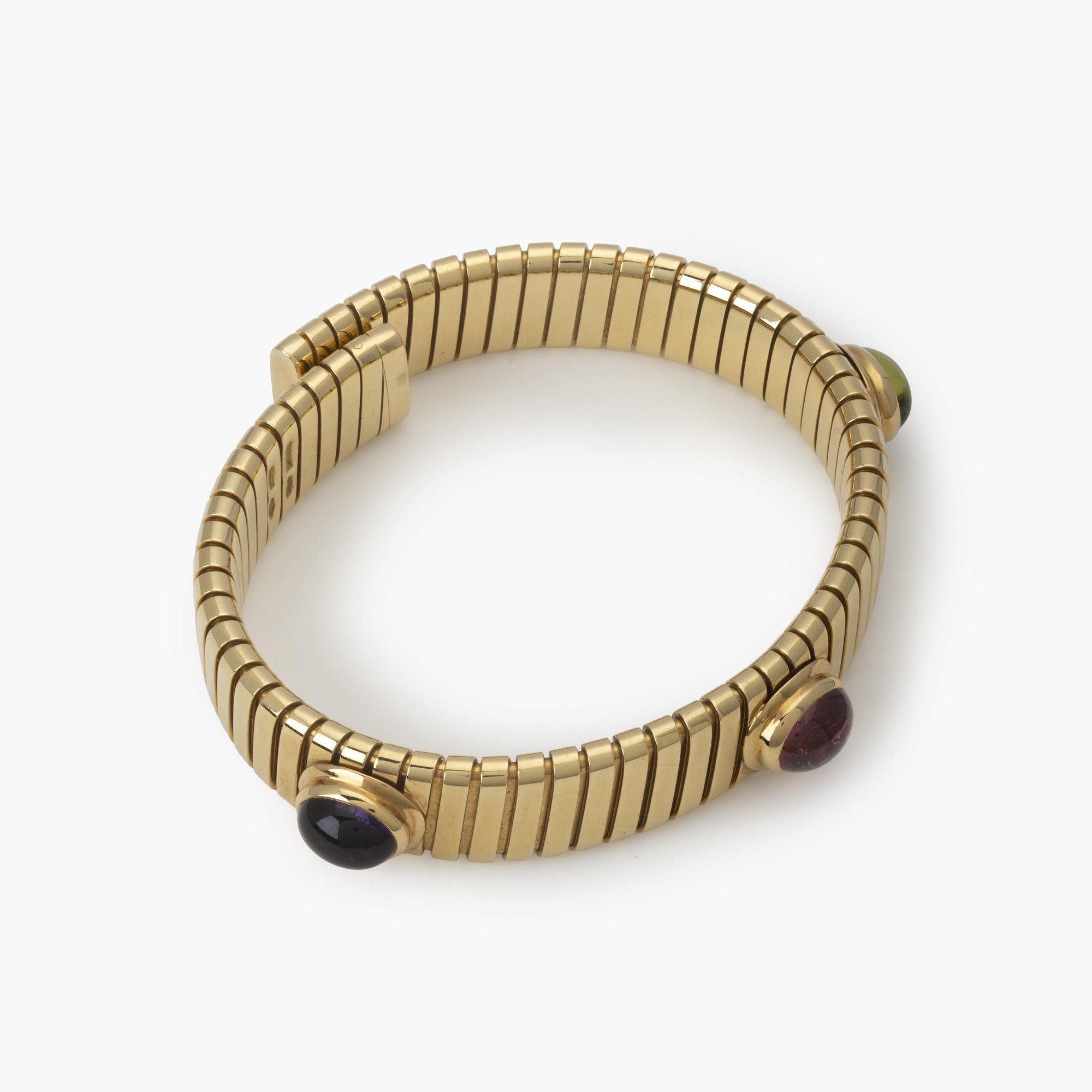 Een achttien karaat geelgouden rechte ‘Tubogas’ span armband, bezet met amethist, toermalijn en peridot. Gesigneerd Bvlgari, Italië, omstreeks 1995.